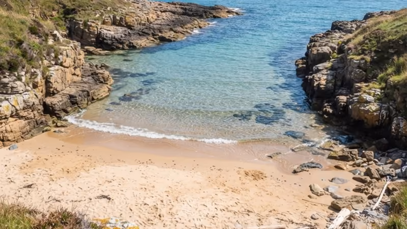 A small rocky cove with clear green water and a fringe of low cliffs