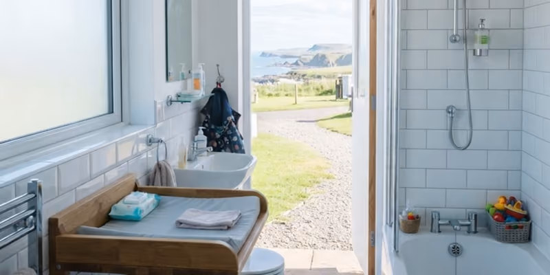 The family room: a changing table and basin under the window, the bath on the right, and the door open to the grass path