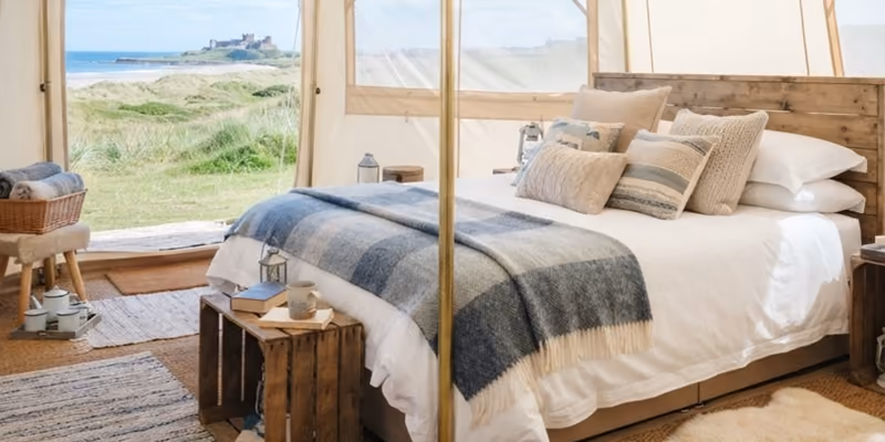 Inside a bell tent, the bed made up with linen, rugs and cushions