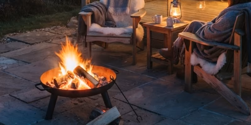 A firepit burning between two deck chairs outside a pod